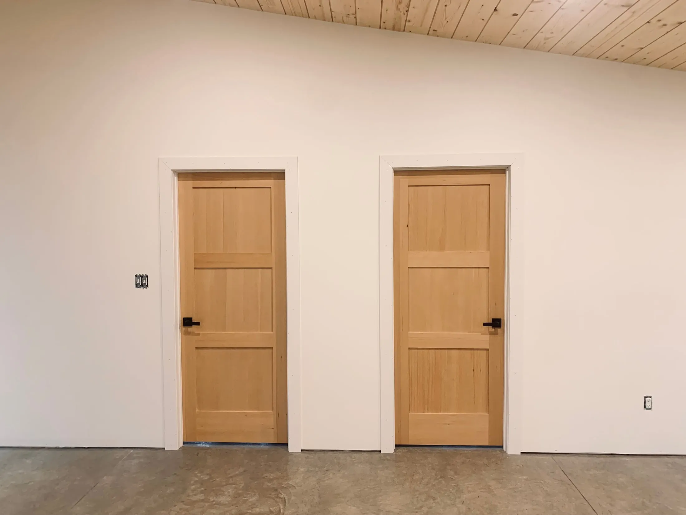 Two solid wood interior doors, hung and cased, under a tongue and groove ceiling